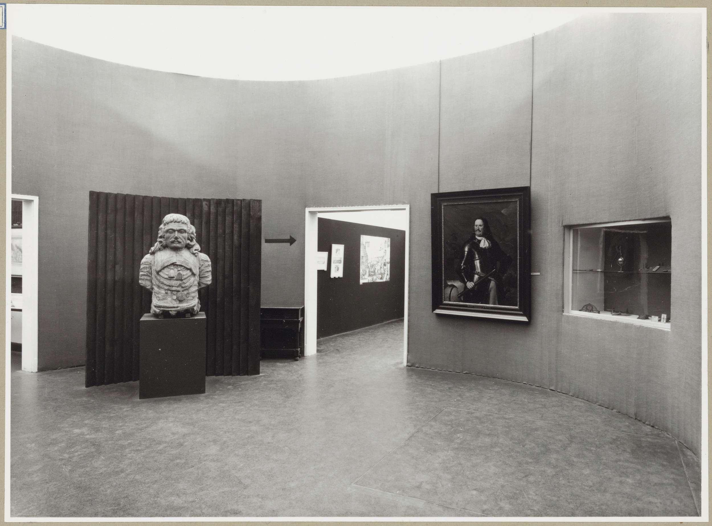 Zaal met een borstbeeld, een schilderij en een vitrine in de muur rechts