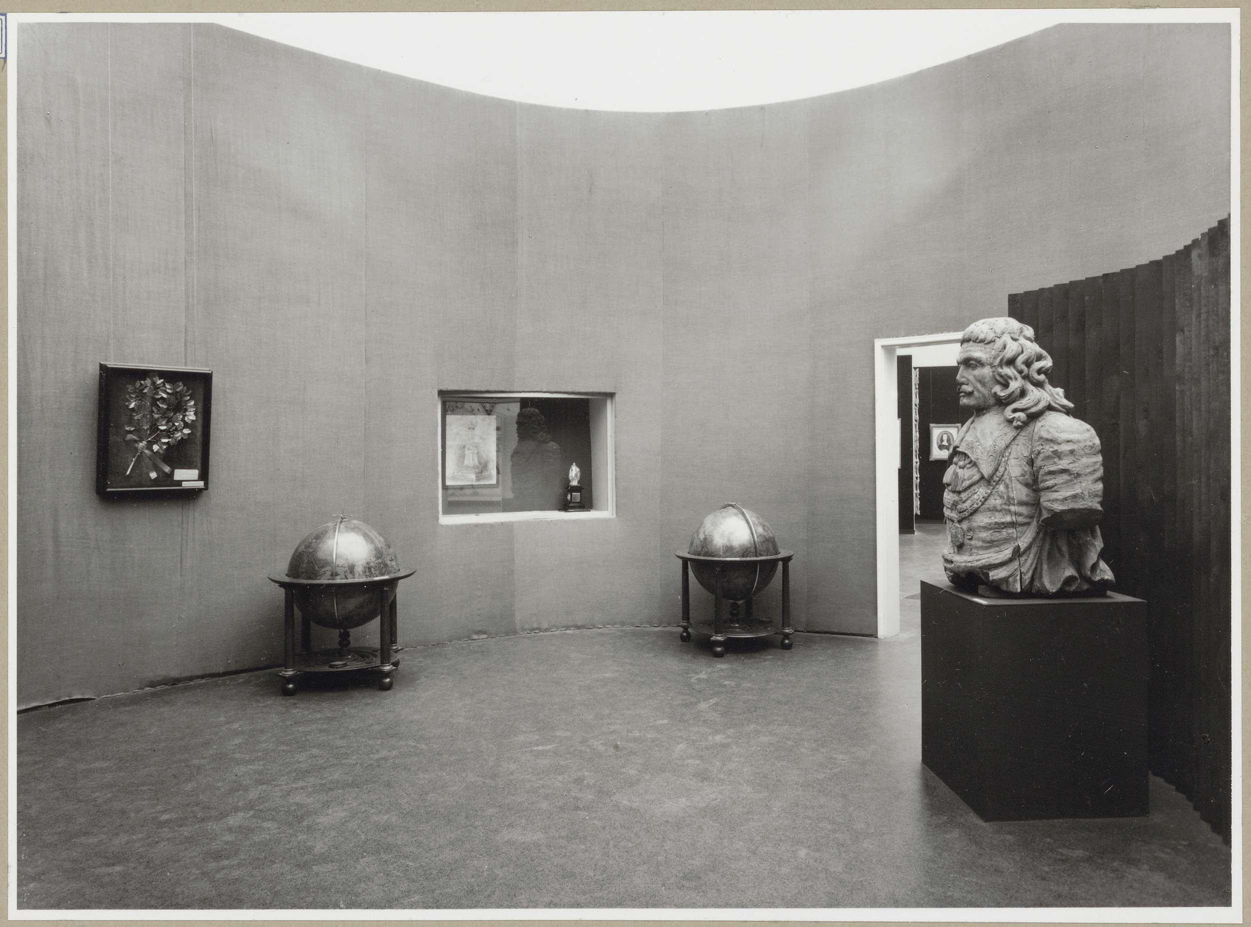 Zaal met een aard- en hemelglobe aan weerszijden van een vitrine, rechts staat een borstbeeld