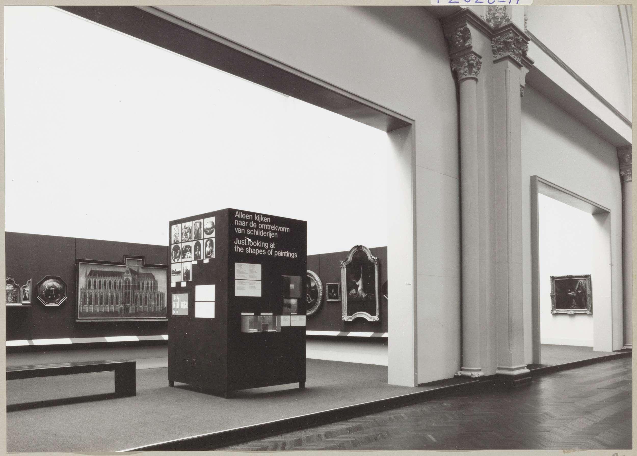 Kabinet van de Eregalerij met diverse objecten, een informatiepaneel met de tentoonstellingstitel, een bank voor bezoekers en zicht op een naastgelegen kabinet