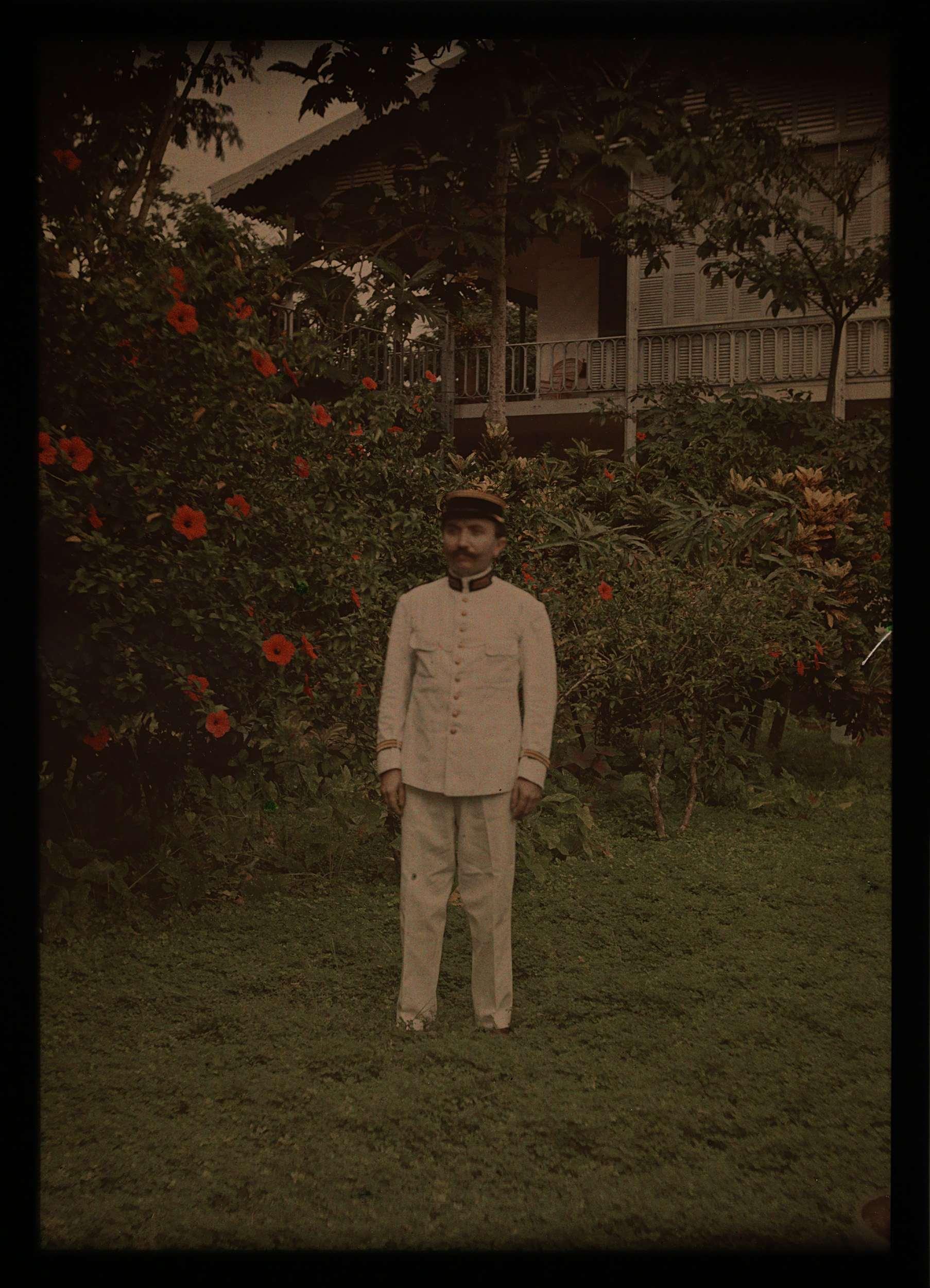Man in uniform, in tuin met op de achtergrond een huis