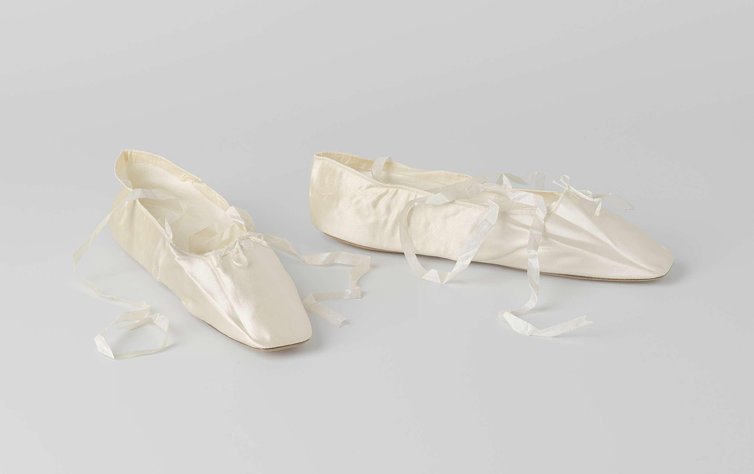 Bruidsschoen plat model met enkelband en dunne witte zijden linten van crème satijn, versierd met een kleine witte satijnen strik